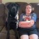 girl sitting on sofa next to black Lab service dog, both are looking at camera