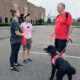 man with black Standard Poodle service dog standing in parking lot talking with two young women