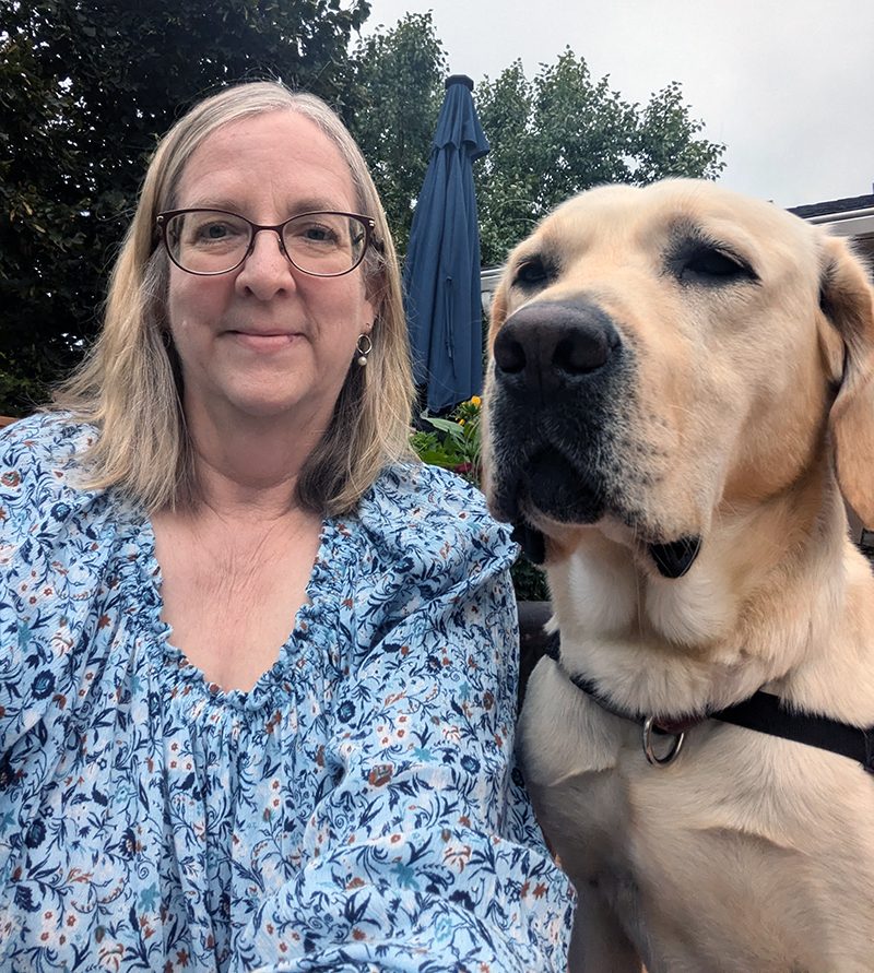 woman outside with arm around yellow Lab dog, smiling at camera