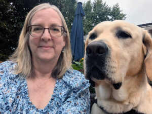 woman outside with arm around yellow Lab dog, smiling at camera