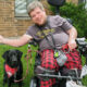 man sitting outside in power chair next to black Lab service dog, both are smiling at camera