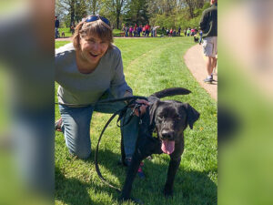 woman kneels next to her black Lab.