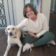 woman sitting on hardwood floor with hand on yellow Lab; both are smiling at the camera